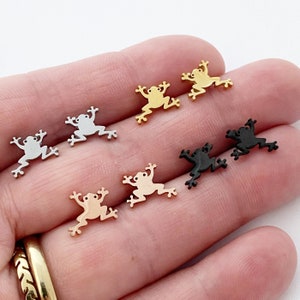May include: A set of seven frog charms in various colors, including silver, gold, rose gold, and black. The charms are made of metal and have a detailed frog design.