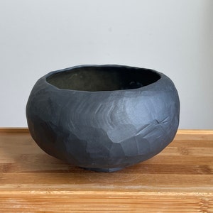 May include: A black ceramic bowl with a rough, textured surface. The bowl is round and has a wide opening.