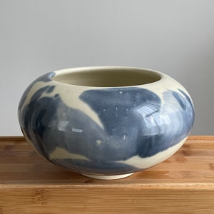May include: A white ceramic bowl with a blue and white marbled glaze. The bowl is round and has a wide opening.