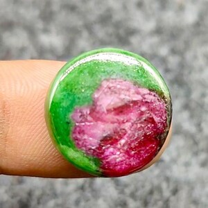 Pode incluir: Uma pedra preciosa redonda com uma combinação de cores vibrantes. A parte superior da pedra apresenta um tom verde brilhante, que se transforma num centro rosa e vermelho intenso. A superfície polida reflete a luz, realçando a beleza natural.