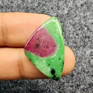Pode incluir: Uma pedra preciosa polida com formato triangular. A pedra apresenta um exterior verde vibrante com uma área central de vermelho profundo. Pequenas inclusões pretas são visíveis nas áreas verdes.