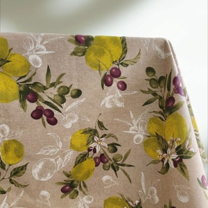 May include: A beige linen tablecloth with a repeating pattern of lemons, olives, and olive branches. The lemons are yellow and the olives are purple.