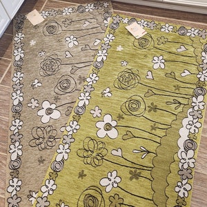 May include: Two rectangular area rugs with floral designs. The rug on the left is brown with white flowers and the rug on the right is green with white flowers.