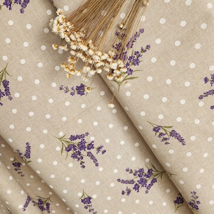 May include: Beige fabric with white polka dots and purple lavender sprigs. A bundle of dried flowers rests on the fabric. The fabric is folded, showing the pattern and texture. Ideal for home decor or crafting projects.