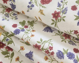 Könnte beinhalten: Weißer Stoff mit einem Blumenmuster mit roten, gelben und blauen Blumen. Der Stoff ist dreifach gefaltet, sodass das Muster auf jeder Schicht sichtbar ist.