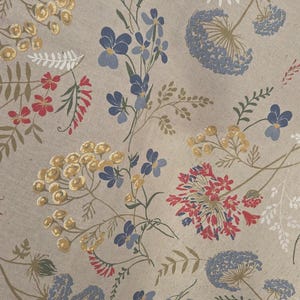 May include: A beige fabric with a floral pattern featuring blue, red, and yellow flowers. The design includes various flower types and green stems, creating a natural, botanical theme. The fabric has a textured appearance.