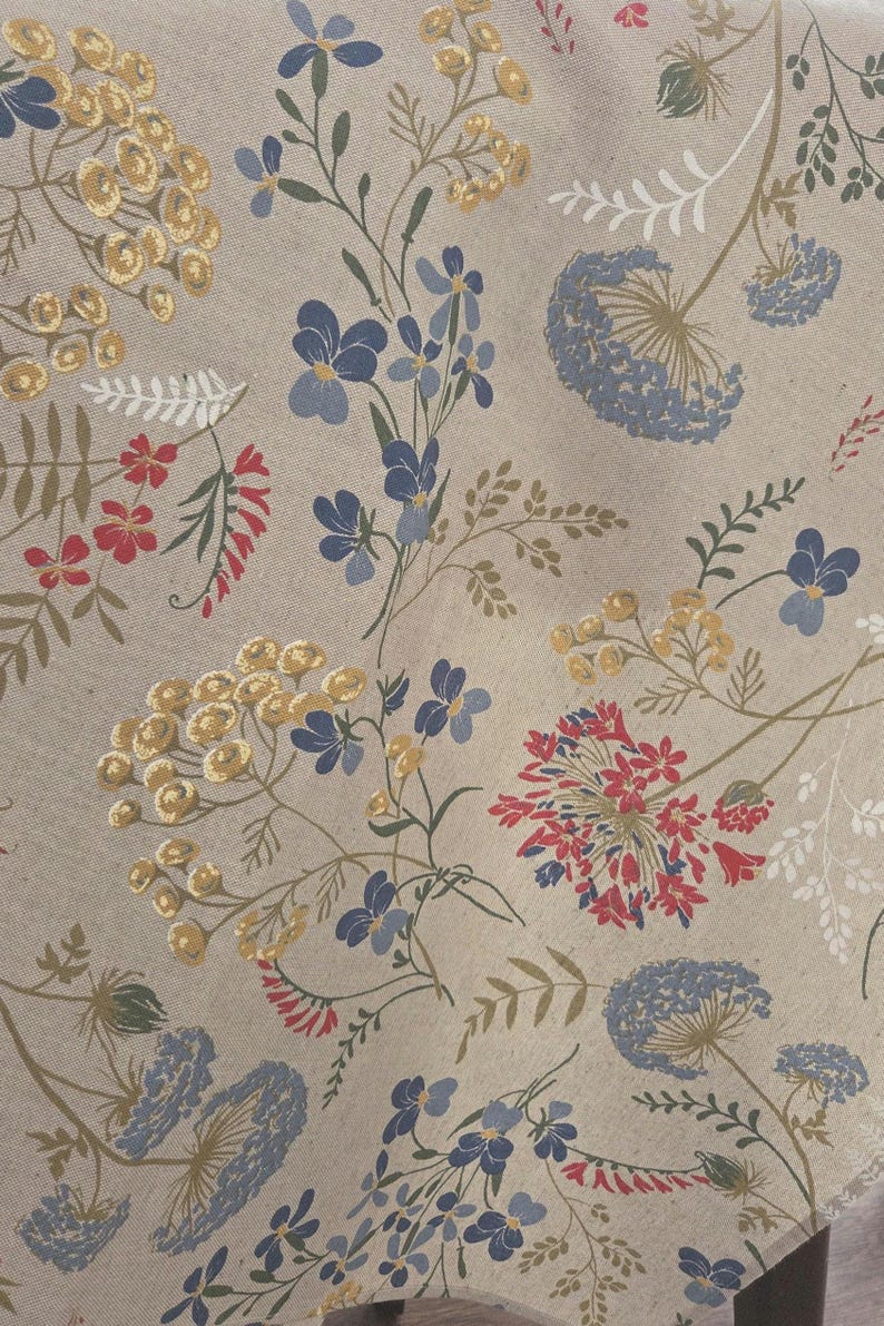 May include: A beige fabric with a floral pattern featuring blue, red, and yellow flowers. The design includes various flower types and green stems, creating a natural, botanical theme. The fabric has a textured appearance.