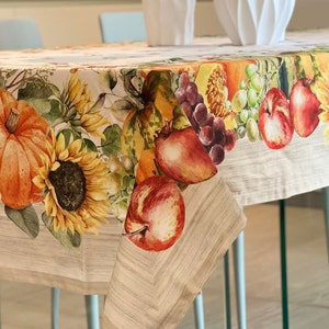 Puede incluir: Un mantel beige con un tema de cosecha de otoño. El mantel presenta un borde de frutas, verduras y girasoles pintados. El mantel está hecho de una tela suave y duradera y es perfecto para agregar un toque de encanto otoñal a su mesa de comedor.