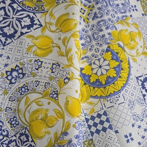 May include: White fabric featuring a repeating pattern of yellow lemons and blue and white decorative tiles. The lemons are clustered with green leaves. Tile designs include floral and geometric patterns.