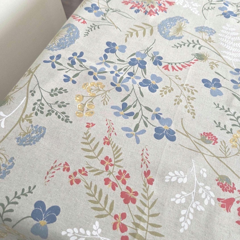 Close-up fabric texture: linen-look weave, multicolor wildflowers on warm beige-tan background, cotton blend.