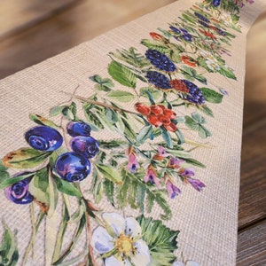 Op de afbeelding: Een beige tafelkleed met een bloemenmotief met blauwe bessen, bramen en rode bessen. Het ontwerp is in aquarelstijl en bevat groene bladeren en witte bloemen.