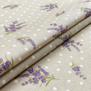 May include: Beige fabric with a repeating pattern of purple lavender sprigs and white polka dots. The fabric is folded, showing the texture and design. The lavender has green stems and leaves.