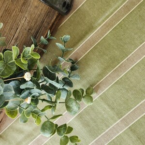 K&ouml;nnte beinhalten: Nahaufnahme einer gr&uuml;n-wei&szlig; gestreiften Tischdecke mit einem Strau&szlig; getrockneter wei&szlig;er Blumen und gr&uuml;nen Eukalyptusbl&auml;ttern.