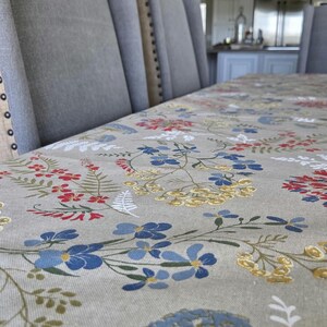 May include: A dining table set with upholstered gray chairs and a floral tablecloth. The tablecloth features a pattern of red, blue, and yellow flowers on a neutral background. The chairs have button detailing.