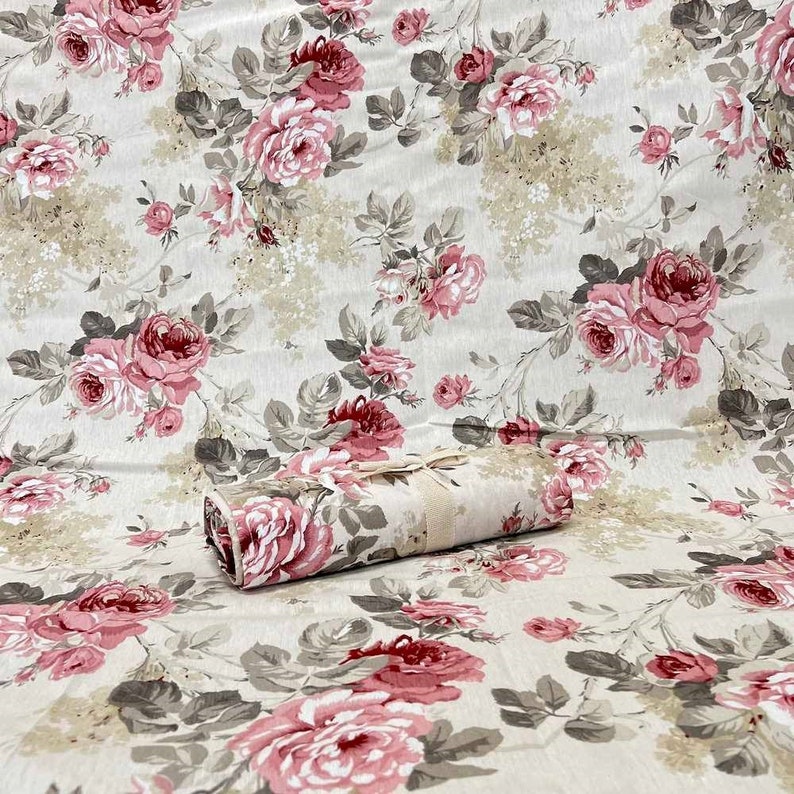 Puede incluir: Un primer plano de una tela beige con un estampado floral rosa y verde. La tela est&aacute; enrollada y atada con una cinta.