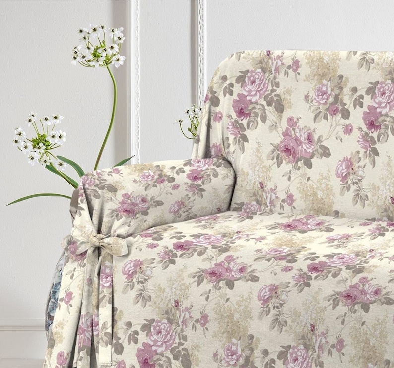Puede incluir: Una funda de sof&aacute; floral con fondo crema y rosas rosas. La funda tiene un lazo en la parte delantera y est&aacute; hecha de un tejido suave y texturizado.