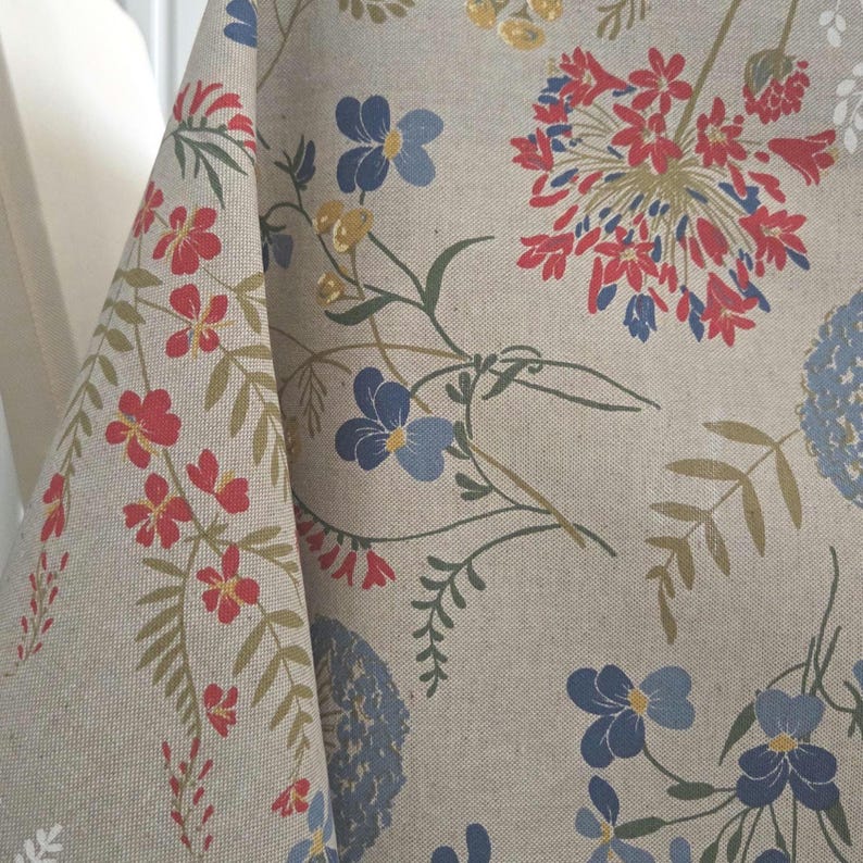 Corner drape detail showing hem and fall, beige-tan base with blue and red flowers, easy-care cotton blend.