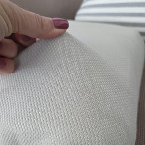 May include: Close-up of a light gray textured fabric, possibly upholstery material. The fabric has a subtle, repeating pattern and a soft appearance. The texture is visible, with a slight sheen. The image focuses on the fabric's surface.