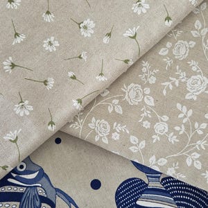May include: Close-up of three different fabric patterns. One features small white flowers with green stems on a tan background. Another has white roses and vines on a tan background. The third has blue fish.