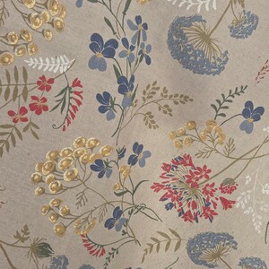 May include: A beige fabric with a floral pattern featuring blue, yellow, and red flowers. The design includes various flower types and green stems, creating a natural, botanical theme. The fabric is likely used for home decor or textiles.