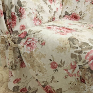Puede incluir: Una funda de sof&aacute; beige con un estampado floral con rosas rosas y rojas. La funda tiene una falda fruncida y lazos en la parte delantera.
