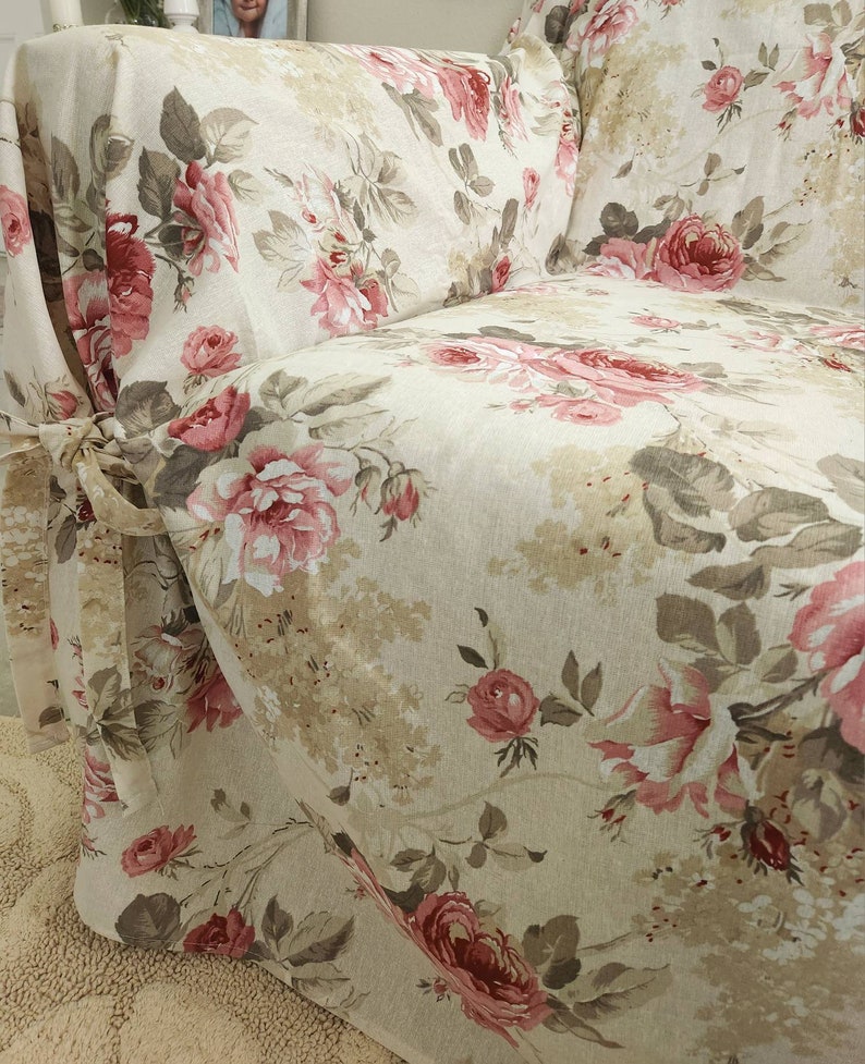 Puede incluir: Una funda de sof&aacute; beige con un estampado floral con rosas rosas y rojas. La funda tiene una falda fruncida y lazos en la parte delantera.