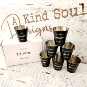 May include: Set of seven black shot glasses with gold lettering. The glasses are arranged in a pyramid shape. The glasses are engraved with the names "Nathaniel", "Andrey", "James", "Seth", "Raj", "Adrian", and "Joshua" and the date "10.18.24".
