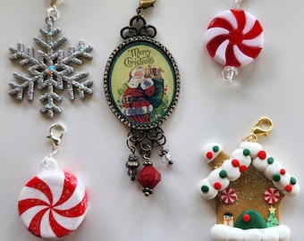 May include: A collection of Christmas-themed charms. Includes a silver snowflake, a charm with a Santa Claus image and the text "Merry Christmas", two red and white peppermint candy charms, and a gingerbread house charm.
