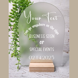 May include: White frosted acrylic sign with rounded top and a wooden stand. The sign says "Your Text can go anywhere on the sign BUSINESS SIGN or SPECIAL EVENTS 02.14.2025".