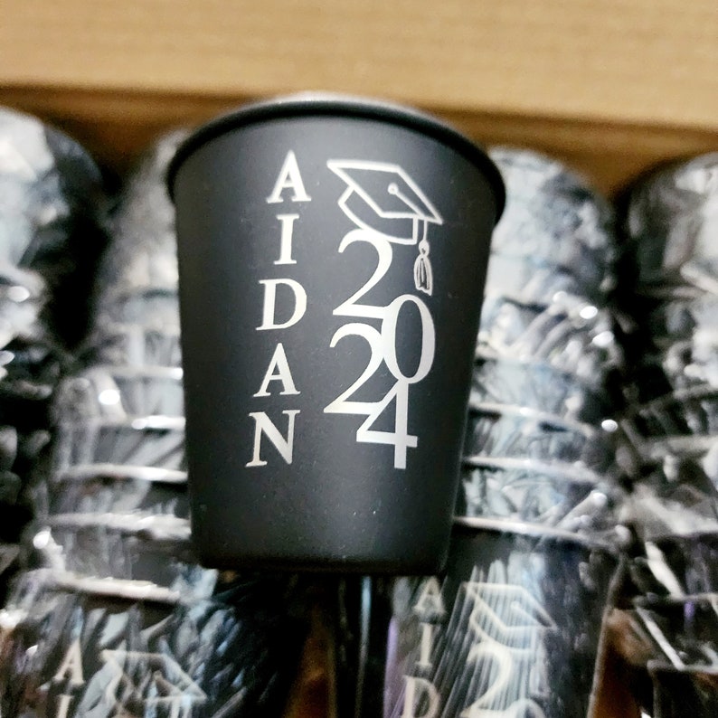 May include: Black plastic shot glass with the name "AIDAN" and the year "2024" printed in silver, along with a graduation cap graphic.
