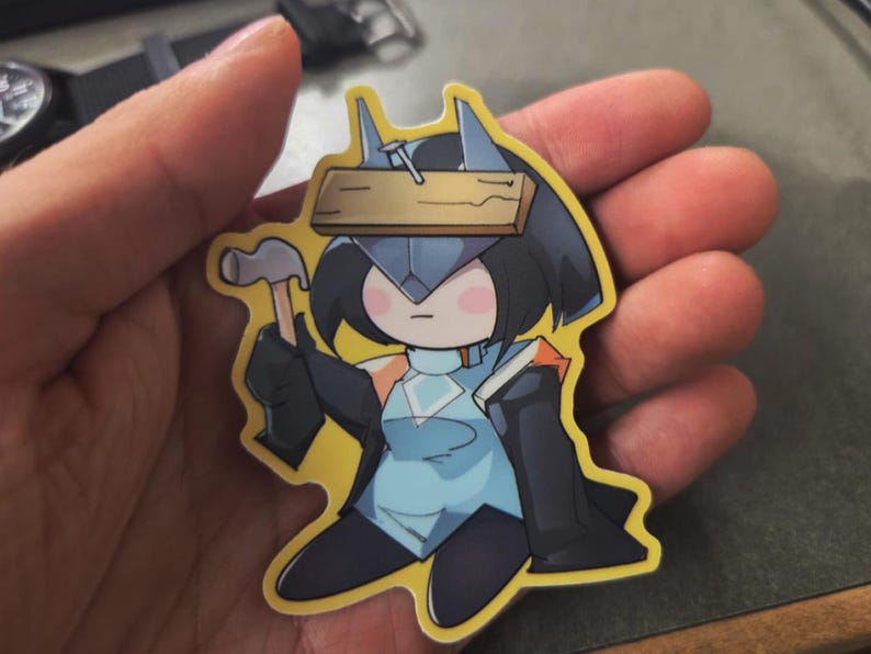 May include: A sticker featuring a cartoon character in a blue and black outfit, holding a hammer and a book. The character has a wooden plank with a nail on their head. The sticker has a yellow border.