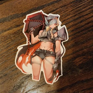 Könnte beinhalten: Ein Aufkleber mit einer weiblichen Figur mit blonden Haaren, die ein Kapuzenoutfit und eine Rüstung trägt und eine große rote Kiste mit einer Kette hält. Die Figur hat einen entschlossenen Ausdruck und steht mit einem leicht gebeugten Bein.