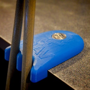 Könnte beinhalten: Ein blauer Pool Queue-Ständer aus Kunststoff mit einem silbernen Logo. Der Ständer ist für zwei Pool Queues ausgelegt.