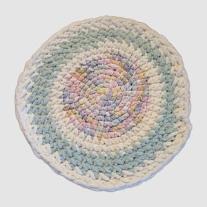 May include: A round, crocheted rug with a pastel swirl design in the center. The rug is white with blue and pink accents.