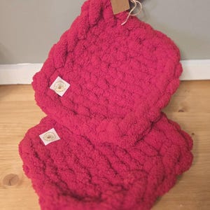 May include: A pair of bright pink, chunky knit pot holders. One pot holder has a loop for hanging and a small tag attached. Each pot holder has a small white label with a bee logo.