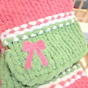 May include: A handmade Christmas stocking in pink and green chunky knit yarn. The stocking features a pink bow applique and white and pink accents. The overall design is festive and cozy, perfect for holiday decor.