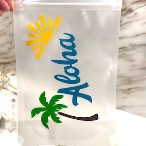May include: A clear plastic reusable drink pouch with a zipper closure. The pouch has a yellow sun with rays, a green palm tree, and the word "Aloha" in blue lettering.