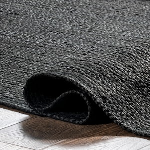 May include: A rolled-up, dark gray woven rug. The rug's texture is visible, with a close-up view highlighting the woven fibers. The rug is on a wooden surface, with the rolled edge creating a shadow.