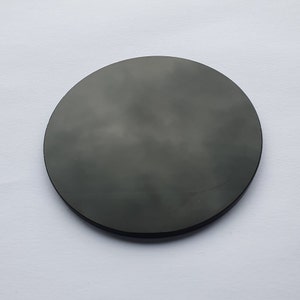 May include: A dark gray, circular object with a smooth surface. The object is set against a white background. The circular shape is clearly defined, and the color appears consistent across the surface.