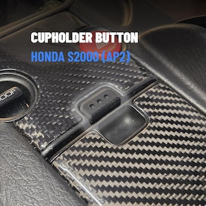 Puede incluir: Primer plano del interior de un coche con un botón de portavasos de fibra de carbono. Los textos "CUPHOLDER BUTTON" y "HONDA S2000 (AP2)" son visibles. También hay un botón rojo.
