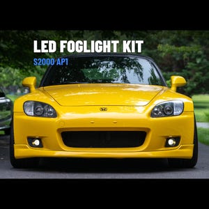 May include: A bright yellow Honda S2000 AP1 sports car featuring an LED foglight kit. The front view displays the vehicle's headlights, a central black grille, and two illuminated fog lights. Text on the image reads LED FOGLIGHT KIT S2000 AP1.