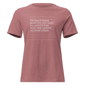 Könnte beinhalten: Kurzärmeliges T-Shirt in Rosé. Auf der Vorderseite steht in weißer Schrift: "Das Ritual des Mähens paralleler Linien wird die existenzielle Angst des Spätkapitalismus und des Klimakollapses nicht lindern."