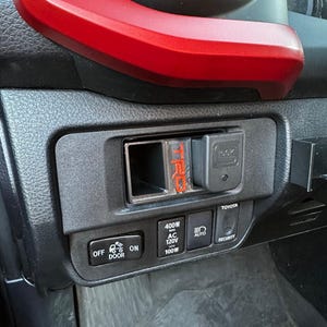 May include: Black dashboard panel with a red accent. Features a TRD logo, a Glock-branded accessory, and various control buttons including "OFF DOOR ON", "400W AC 120V 100W", "AUTO", and "SECURITY".