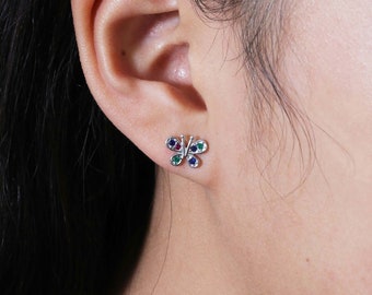 May include: A pair of silver butterfly earrings with green, blue, and red gemstones.