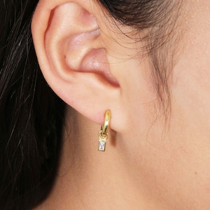 May include: Gold hoop earrings with a small, clear, rectangular stone dangling from each hoop.