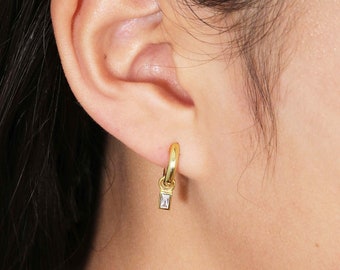 May include: Gold hoop earrings with a small, clear, rectangular stone dangling from each hoop.