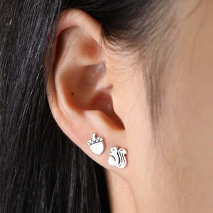 May include: A pair of silver stud earrings featuring a small acorn and a squirrel design.