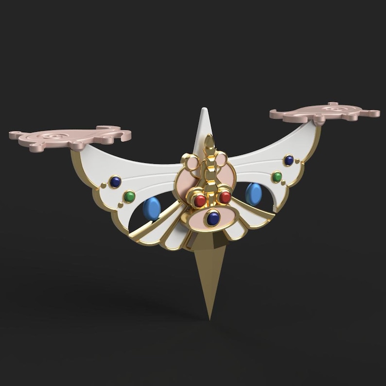 Op de afbeelding: Een gouden en wit vlindervormig decoratief object met rode, blauwe en groene edelstenen. Het object heeft een puntige onderkant en twee vleugels met een roze en wit ontwerp.
