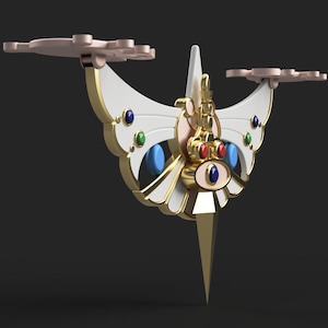 Op de afbeelding: Een gouden en witte decoratieve vlinder met een puntige punt en rode, blauwe en groene edelstenen. De vlinder heeft twee vleugels en een centraal lichaam met een decoratief oogontwerp.