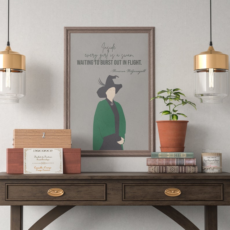 May include: A framed print with a quote by Minerva McGonagall, "Inside every girl is a swan, waiting to burst out in flight." The print features a silhouette of a woman wearing a green robe and a pointed hat. The print is hanging on a wall above a wooden table with a wooden box, a potted plant, and a stack of books.